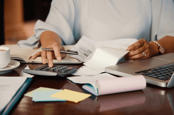 Mulher fazendo o cálculo das despesas usando uma calculadora sobre uma mesa marrom